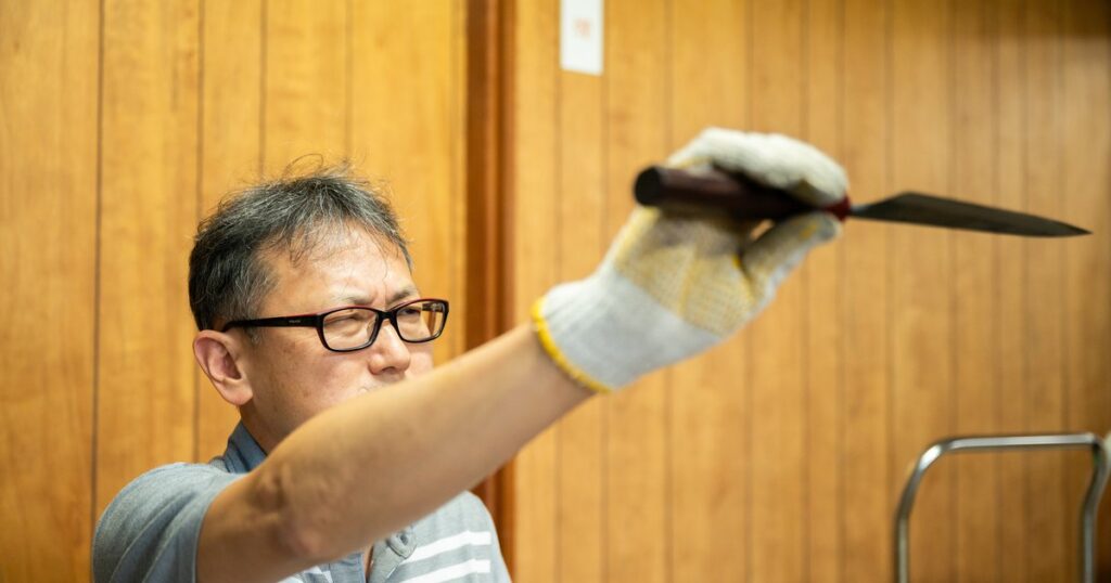 刃をかざして反りや仕上がりを確認する碁盤裕之さん